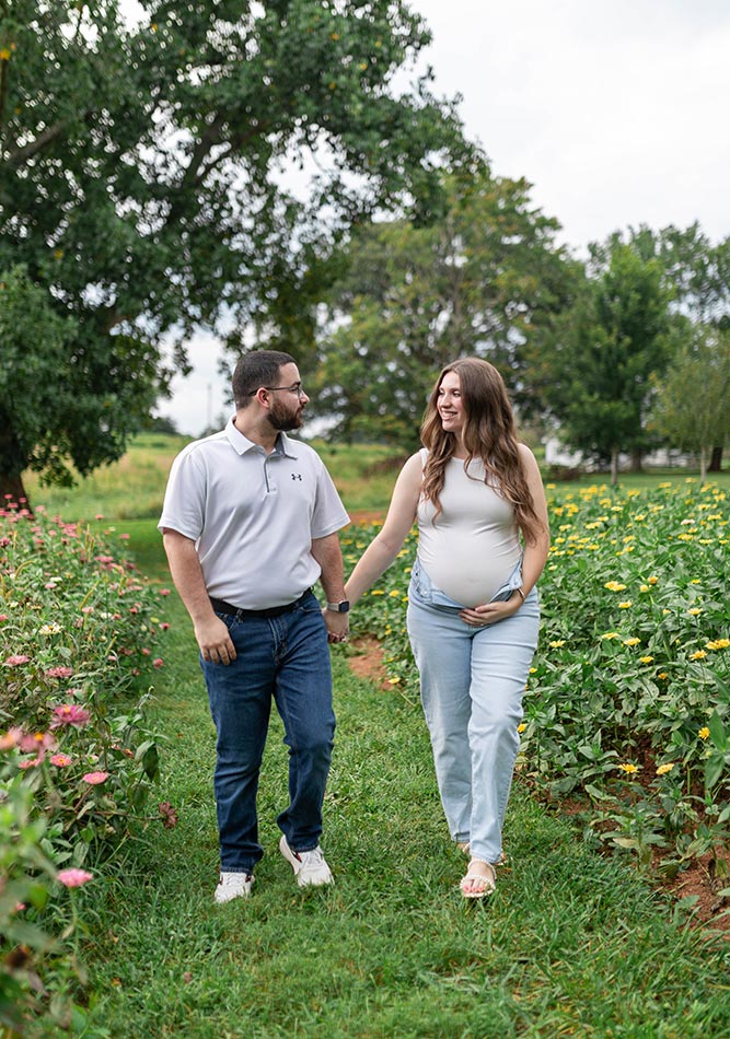 A couple expecting a new baby walking between two zinnia fields at Firefly Haven. Taken by Photography by Melody.